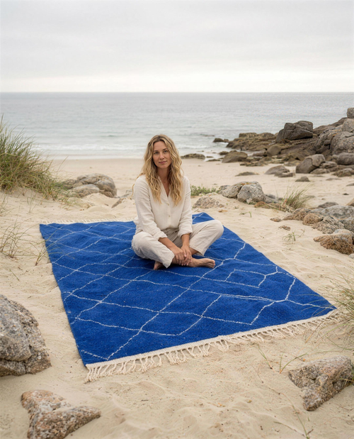 Woman sitting on the blue Beni Ouarain Berber throw on a Breton beach