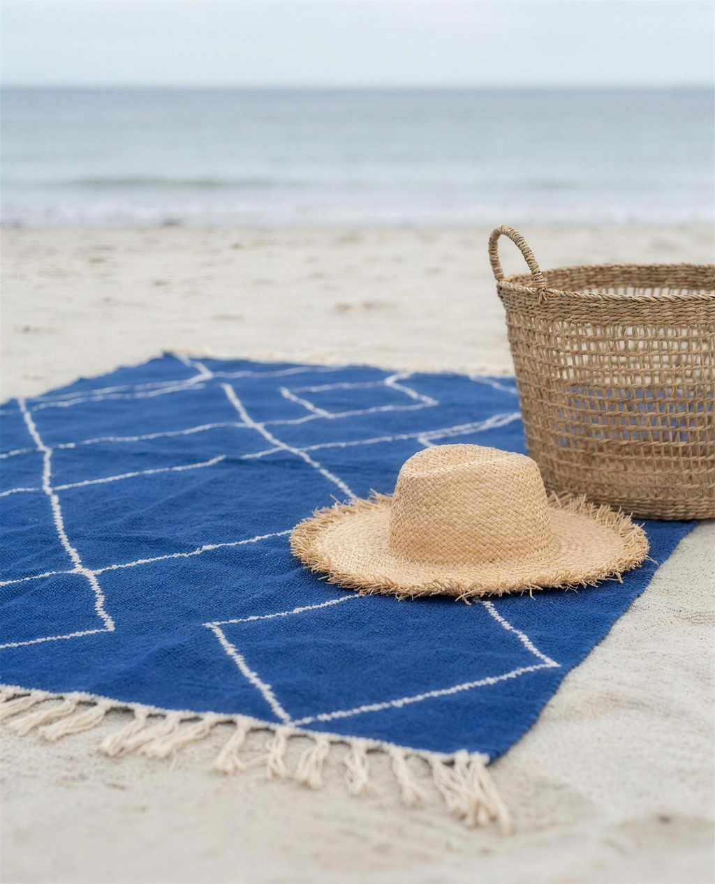 Flat-lay of the blue Beni Ouarain Berber throw on the sand with hat and basket