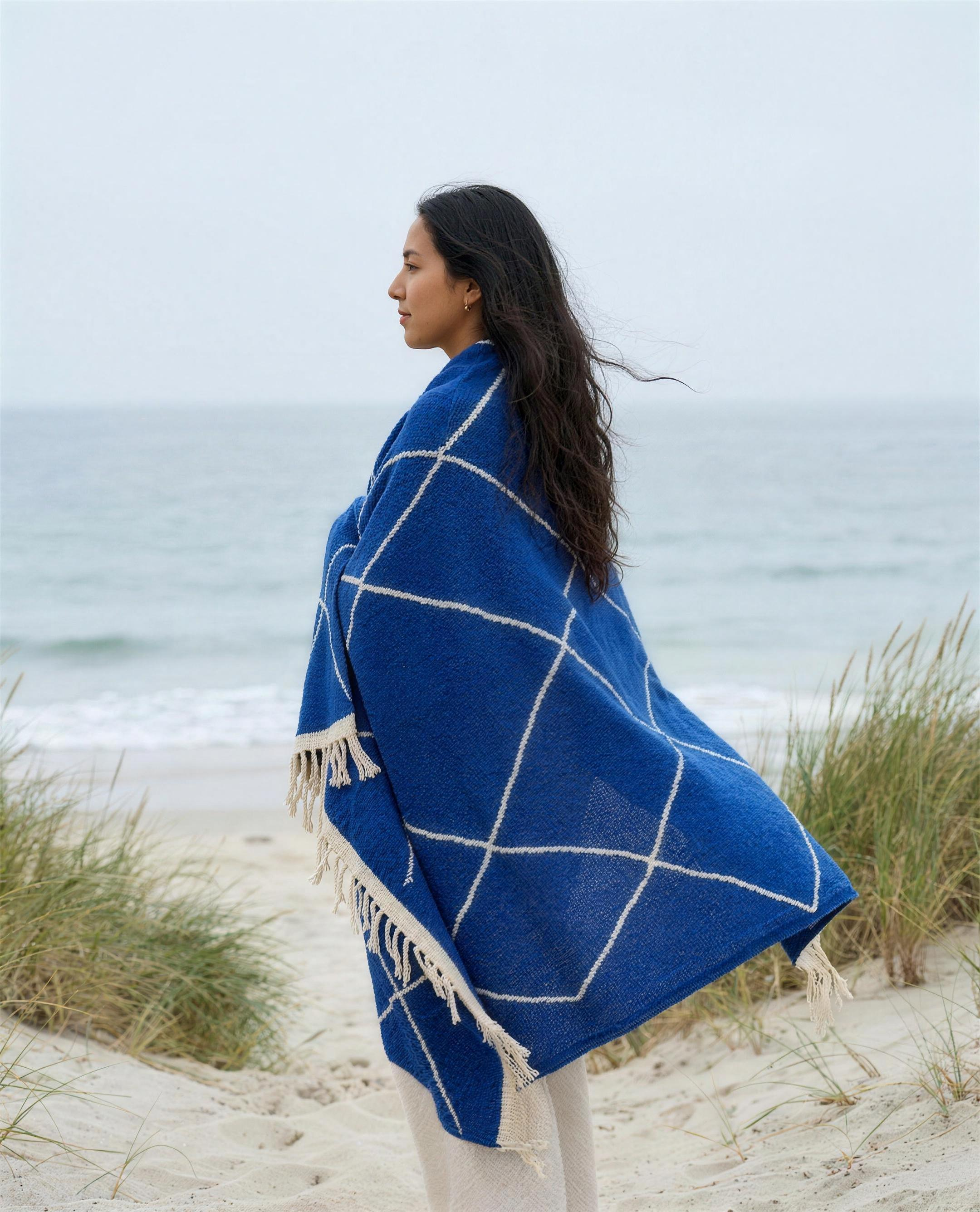 Woman wrapped in the blue Beni Ouarain Berber throw facing the sea