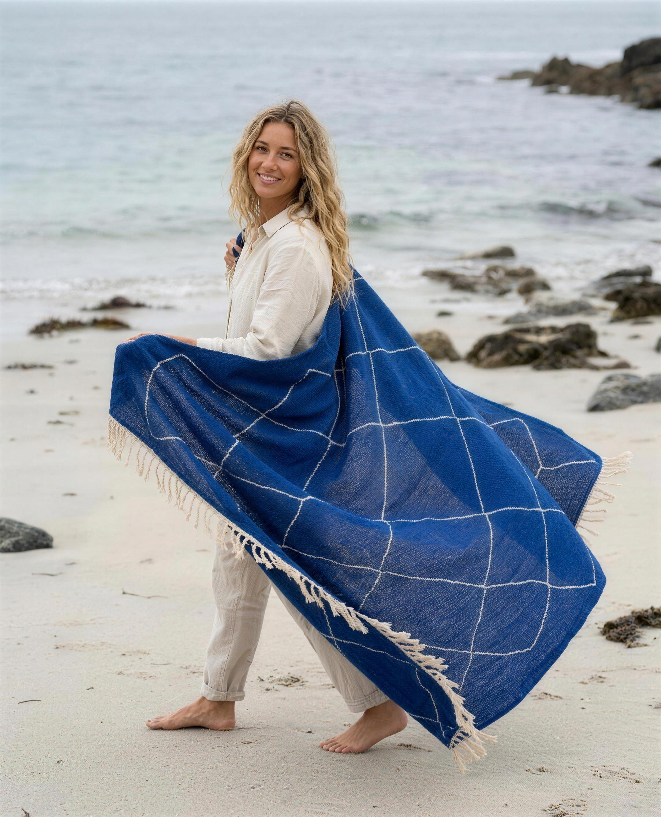 Woman walking on the beach holding the blue Beni Ouarain Berber throw